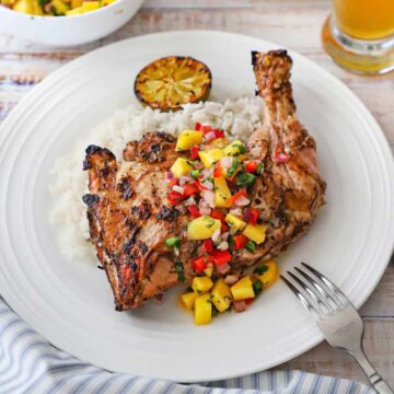 A white dinner plate filled with a serving of Jamaican jerk chicken that is topped with a mango salsa and resting on a bed of coconut rice.