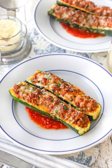 A straight-on view of two white dinner plates filled with two stuffed zucchini boats that are resting on a small layer of marinara sauce.