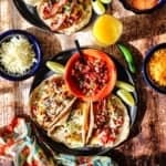 An overhead view of two large black plate filled with breakfast tacos that are stuffed with eggs, chorizo, bacon, potatoes, and sitting next to a bowl of pico de gallo.