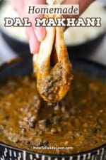 A straight-on view of a person holding a folded piece of naan bread that has been plunged into a bowl of homemade dal makhani and is being held above the bowl with lentils dripping from it.
