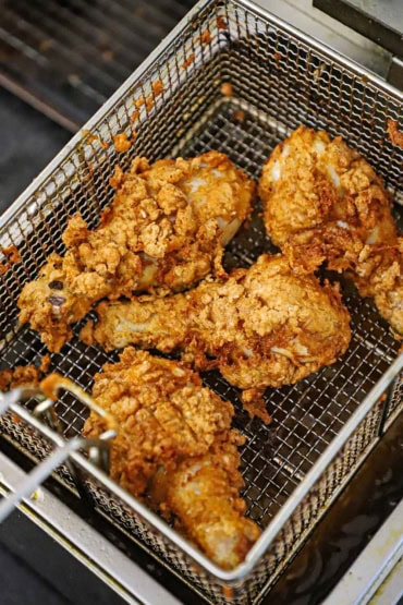 An overhead view of four chicken legs that have been breaded and deep-fried in a deep fryer and are resting in the fryer basket.