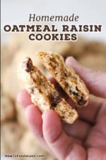 A person holding up a homemade oatmeal raisin cookie that has split in half with the interior of the cookie revealed.
