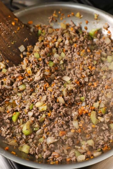 A straight-on view of a cooked ground beef mixture combined with sautéed onions, carrots, celery, and simmered with red wine.