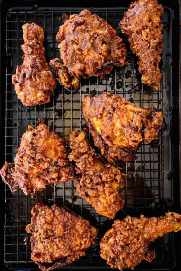 An overhead view of numerous pieces of Nashville hot chicken resting on a baking rack in a baking pan.