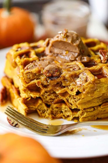 A close-up view a plate of pumpkin waffles with whipped cinnamon honey butter that have been partially eaten with a fork sitting on the plate in front of the waffles.