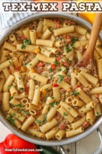 An overhead view of a large stainless steel skillet filled with Tex-Mex pasta with a wooden spoon stuck into the side of it.