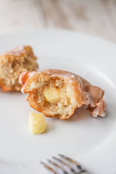 A close-up view of an apple fritter that has been broken in half so the interior is visible including small chunks of cubed apples.