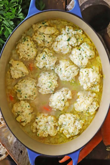 An overhead view of a large oval Dutch oven that is filled with homemade chicken and dumplings soup.