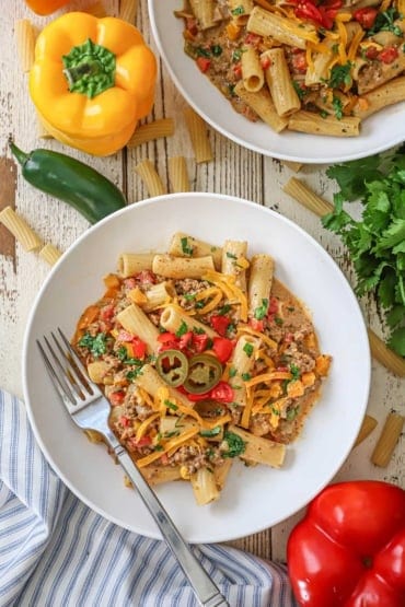 An overhead view of a white bowl filled with a serving of Tex-Mex past topped with chopped cilantro, tomatoes, and a couple slices of pickled jalapeño.