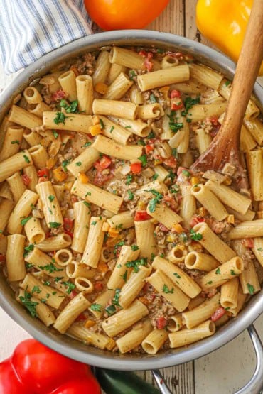 An overhead view of a large stainless steel skillet filled with Tex-Mex pasta with a wooden spoon stuck into the side of it.