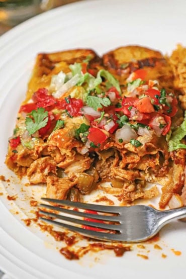 A close-up view of a white dinner plate filled with leftover turkey enchiladas that have been half eaten revealing the turkey on the inside of the tortillas.
