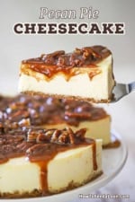 A person using a metal spatula to raise a slice of pecan pie cheesecake from the entire cake resting on a cake stand.