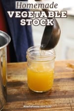 A person using a large wooden ladle to transfer homemade vegetable stock from a stock pan into a glass Mason jar.