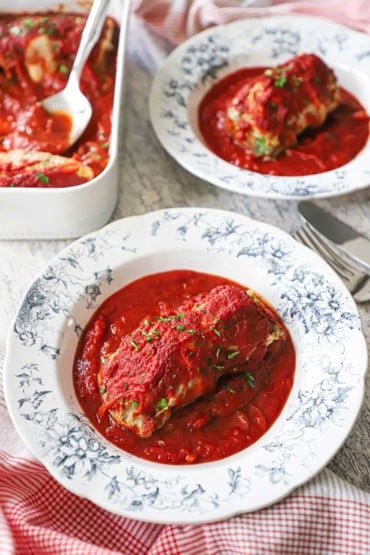Two vintage serving bowl filled with single servings of stuffed cabbage rolls ina rich tomato sauce.