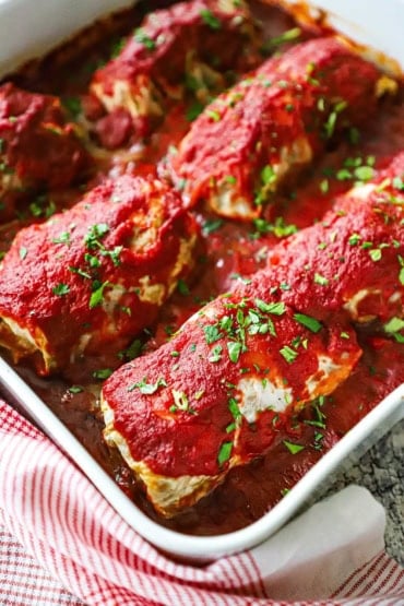 An overhead vide of six stuffed cabbage rolls that have been baked in a square with baking dish with a tomato sauce on top of the rolls and on top, too.