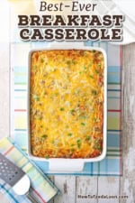An overhead view of best breakfast casserole in a rectangular white baking dish resting on a colorful place matt next to a glass and carafe of orange juice.