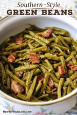 A straight-on view of a white pot that is filled with Southern-style green beans with pieces of cooked bacon intermingled.