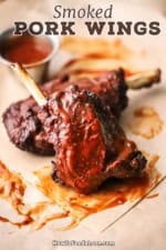 A straight-on view of two pork wings stacked against each other and each have been smoked and then slathered with barbecue sauce.