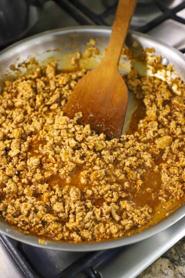 A close-up view of large silver skillet that is filled with cooked ground turkey that is simmering in saucy taco sauce.