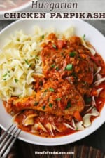 An overhead view of a white shallow bowl holding a serving of chicken paprikash which included two pieces of cooked chicken and topped with a bright red paprika sauce with tomatoes.