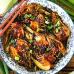 An overhead view of a sautéed baby bok choy resting in a colorful Asian-style bowl with two wooden chopsticks resting on the side of the bowl.