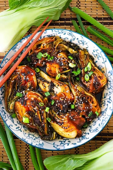 An overhead view of a sautéed baby bok choy resting in a colorful Asian-style bowl with two wooden chopsticks resting on the side of the bowl.