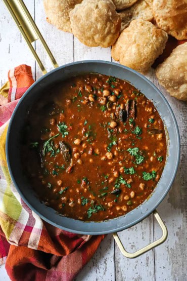 An overhead view of a large, deep skillet filled with chana masala with cooked chickpeas visible and chopped cilantro scattered on top.