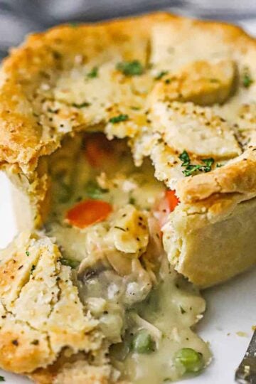 A close-up view of a homemade chicken pot pie with an upper crust and a lower crust that has been broken open with the innards pouring out onto the plate.
