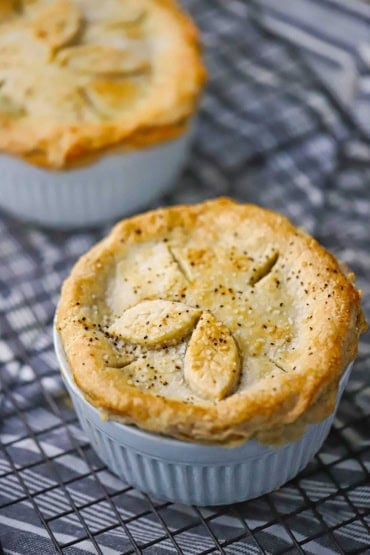 A close-up view of a homemade chicken pot pie that is cooling on a wire rack. The pot pie has slits in the top layer of crust and there are two decorative leaves made out of dough on the top, too.