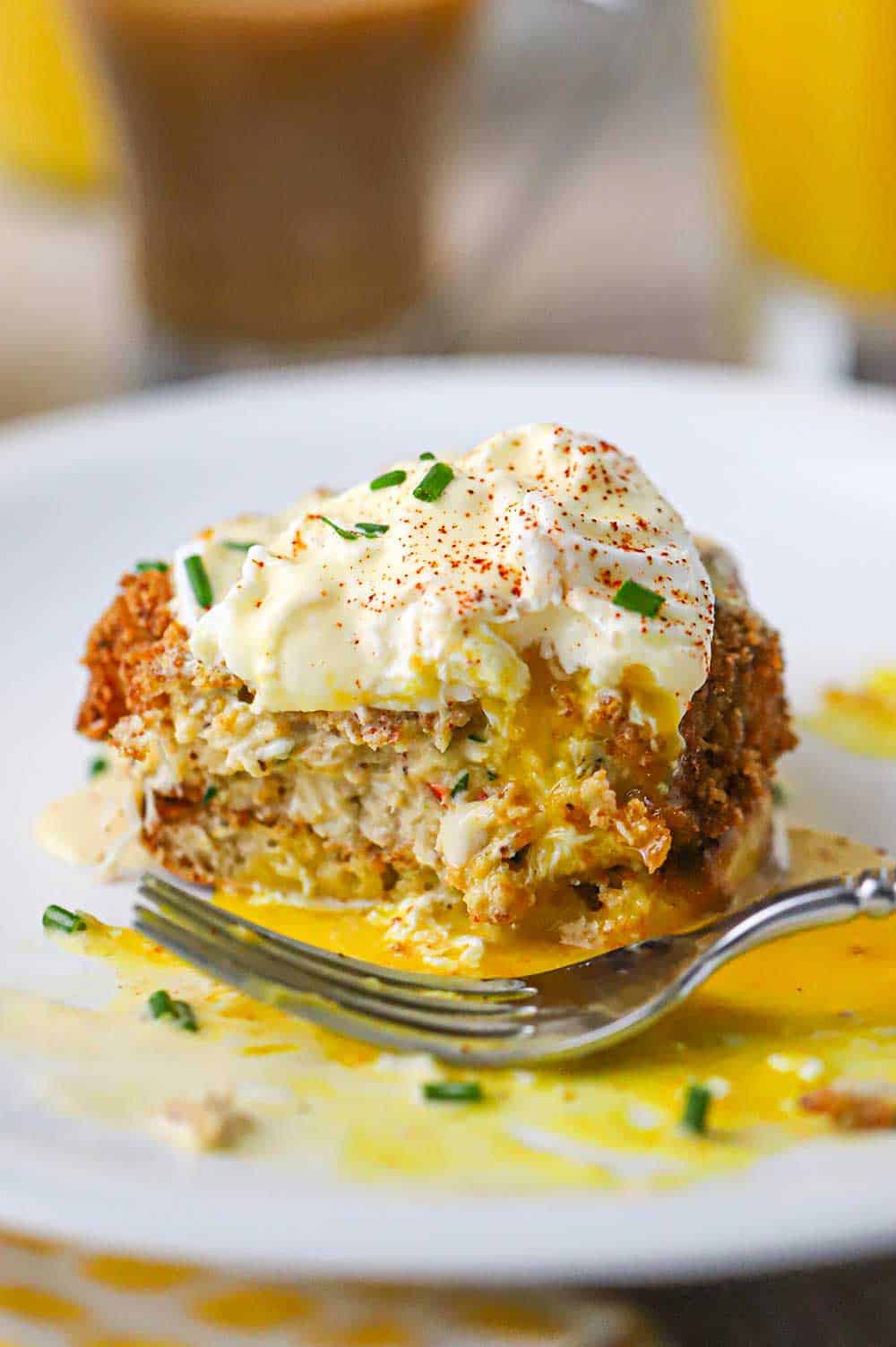 A close-up view of a half-eaten crabs cake Benedict on a white dinner plate sitting in a pool of egg yolk with a fork resting nearby.