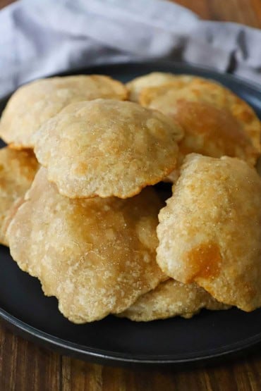 A close-up view of a pile of puffy fried Indian bread called poori and they are sitting on top of each other on a black plate.