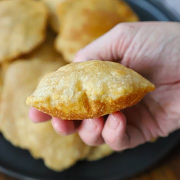 A close-up view of a person holding a puffy Indian fried bread poori in his hand over a black circular platter holding more poori.