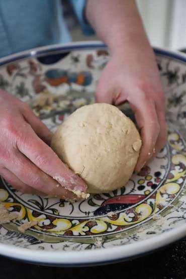 A person holding an orange-shaped ball of poori dough in the middle of a colorful shallow bowl.