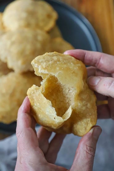 A person using his two hands to open up a freshly fried poori revealing the open interior.