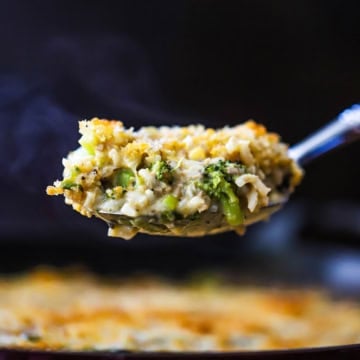A large serving spoon lifting up a helping of broccoli casserole with cheddar and rice over a dish of the same.