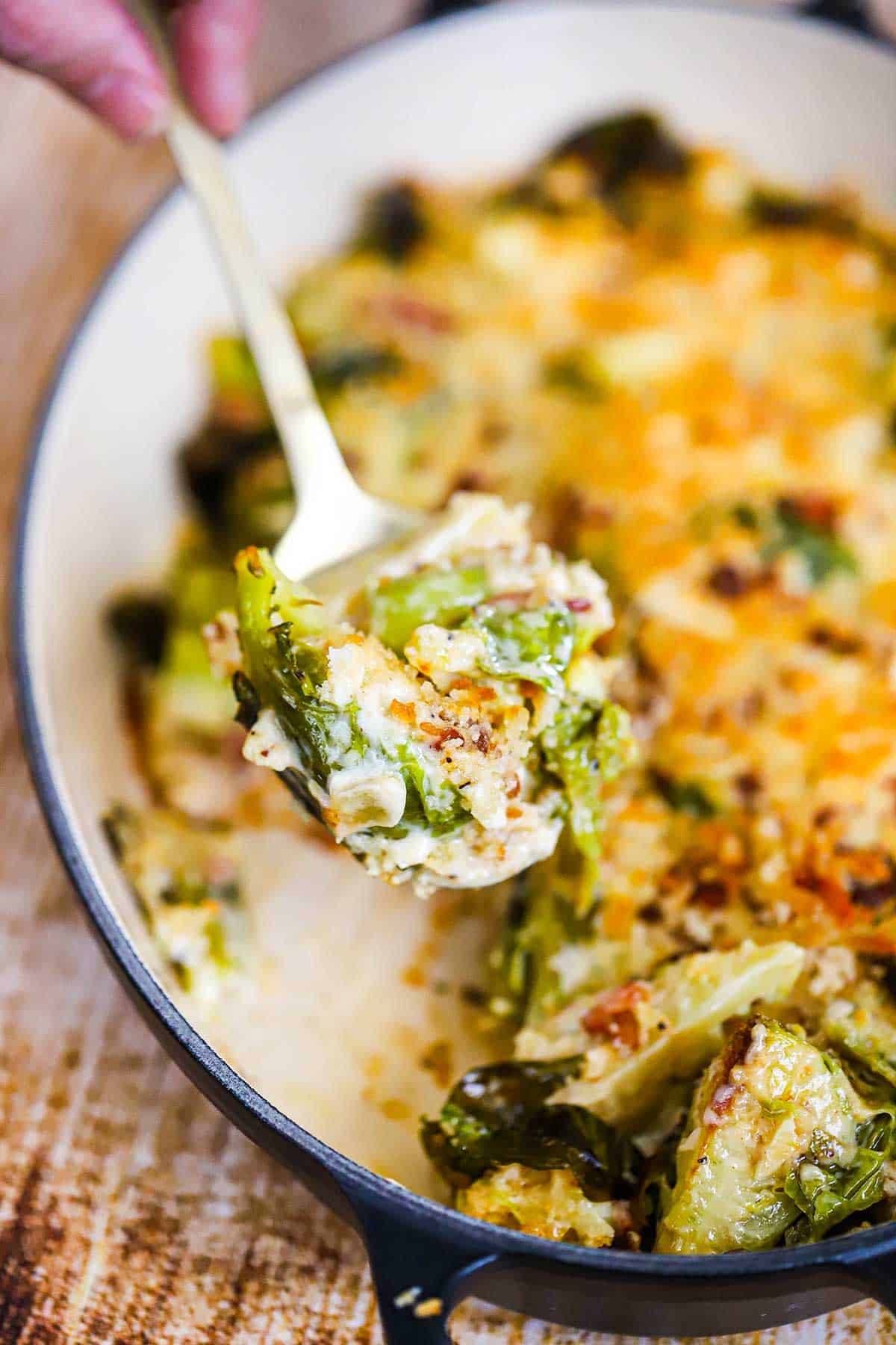 A person raising a serving spoon filled with Brussels sprouts gratin.