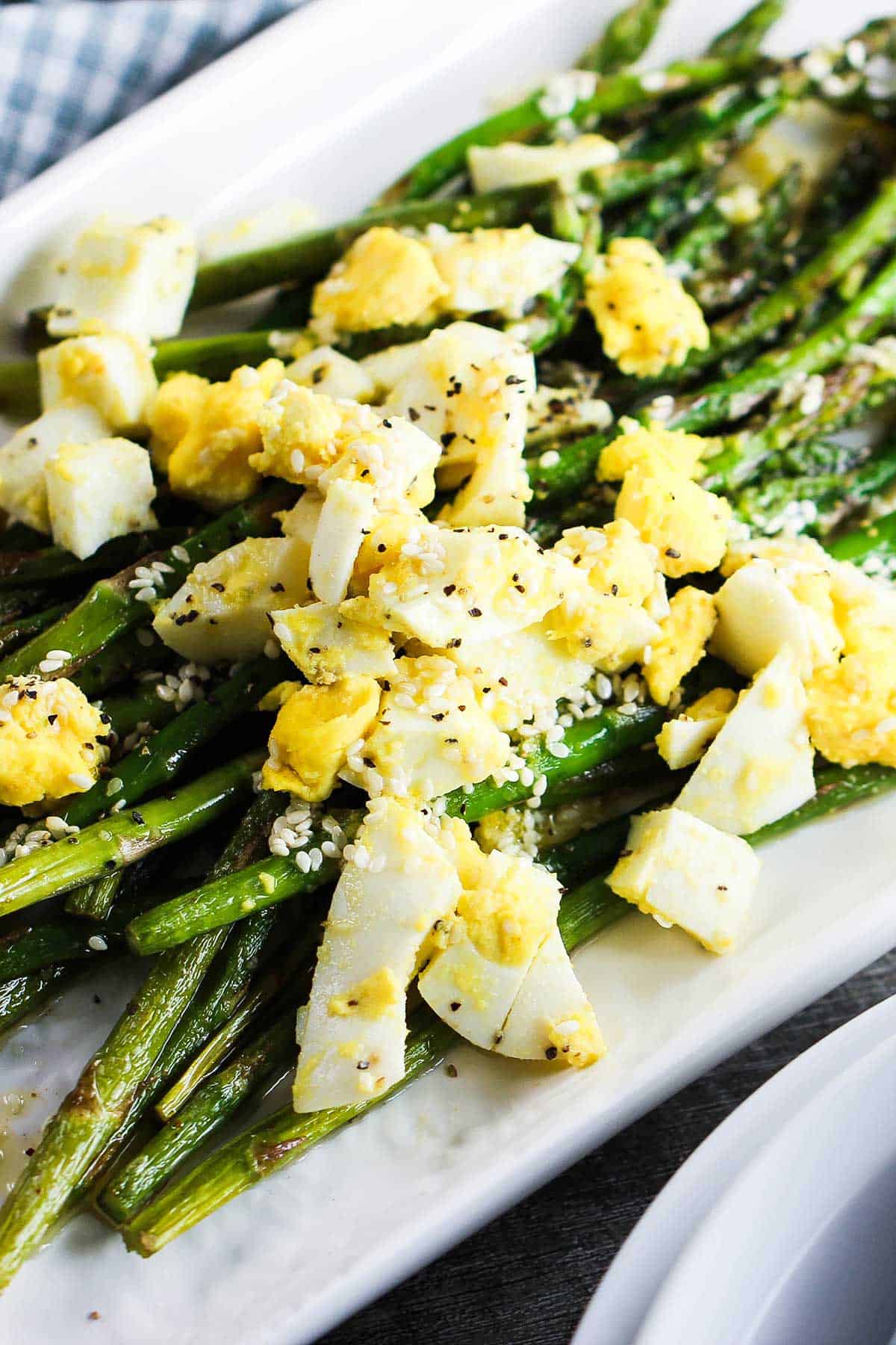 A white platter filled with roasted asparagus with chopped egg on top of the vegetables.