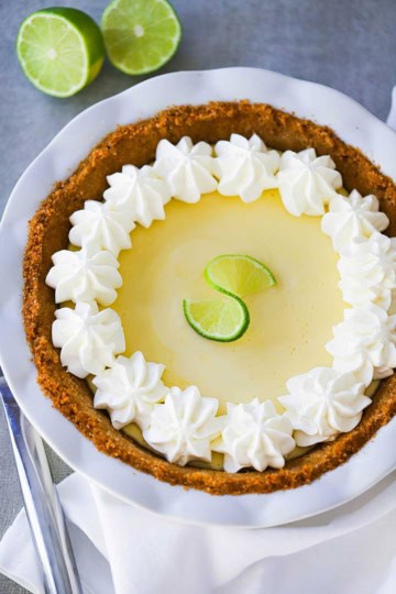 A key lime pie with a graham cracker crust and whipped cream pinwheels along the edges of the top of the pie.
