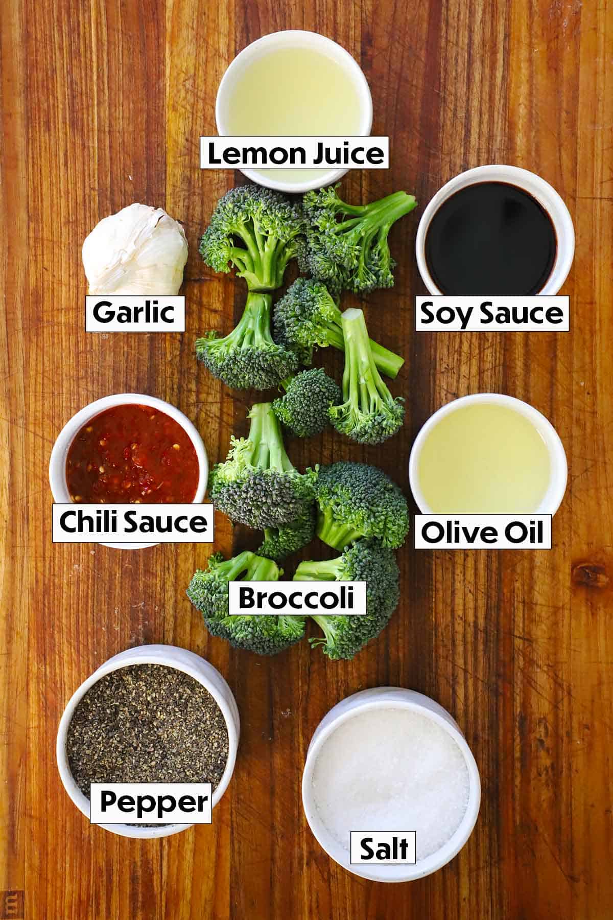 An organized display of ingredients for Roasted Broccoli with a Kick, featuring vibrant broccoli florets, soy sauce, fresh lemon juice, spicy chili sauce, and minced garlic, all arranged on a light background.