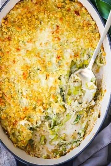 A baking dish filled with a baked leek gratin that has some of it missing and a spoon inserted into the gratin.