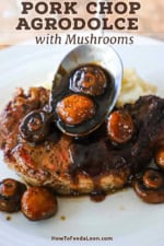 A person spooning an agrodolce sauce with mushrooms over a grilled pork chop on a white dinner plate.