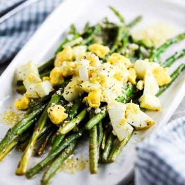 A white platter filled with roasted asparagus with chopped egg on top.