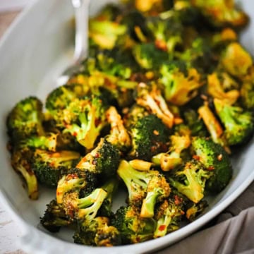 An oval baking dish filled with roasted broccoli with kick and a spoon inserted into the dish.