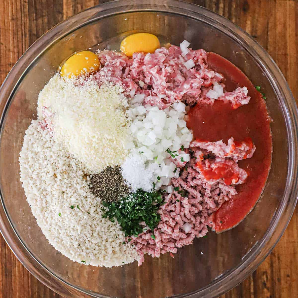 A large glass bowl filled with ground pork and ham, breadcrumbs, eggs, and seasonings for glazed ham loaf.