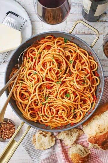 A large, deep skillet filled with Bucatini all’Amatriciana with a block of cheese nearby.