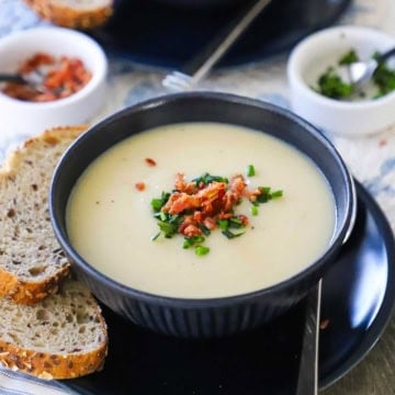 A blue soup bowl filled with creamy Irish potato soup and garnished with crumbled bacon and snipped chives.
