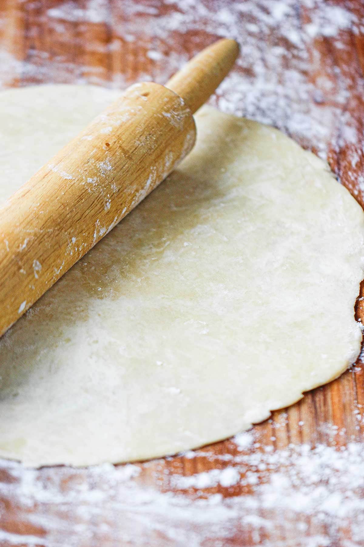 A wooden rolling pin resting on a circular easy pie crust dough that has been rolled out on a floured wooden surface.
