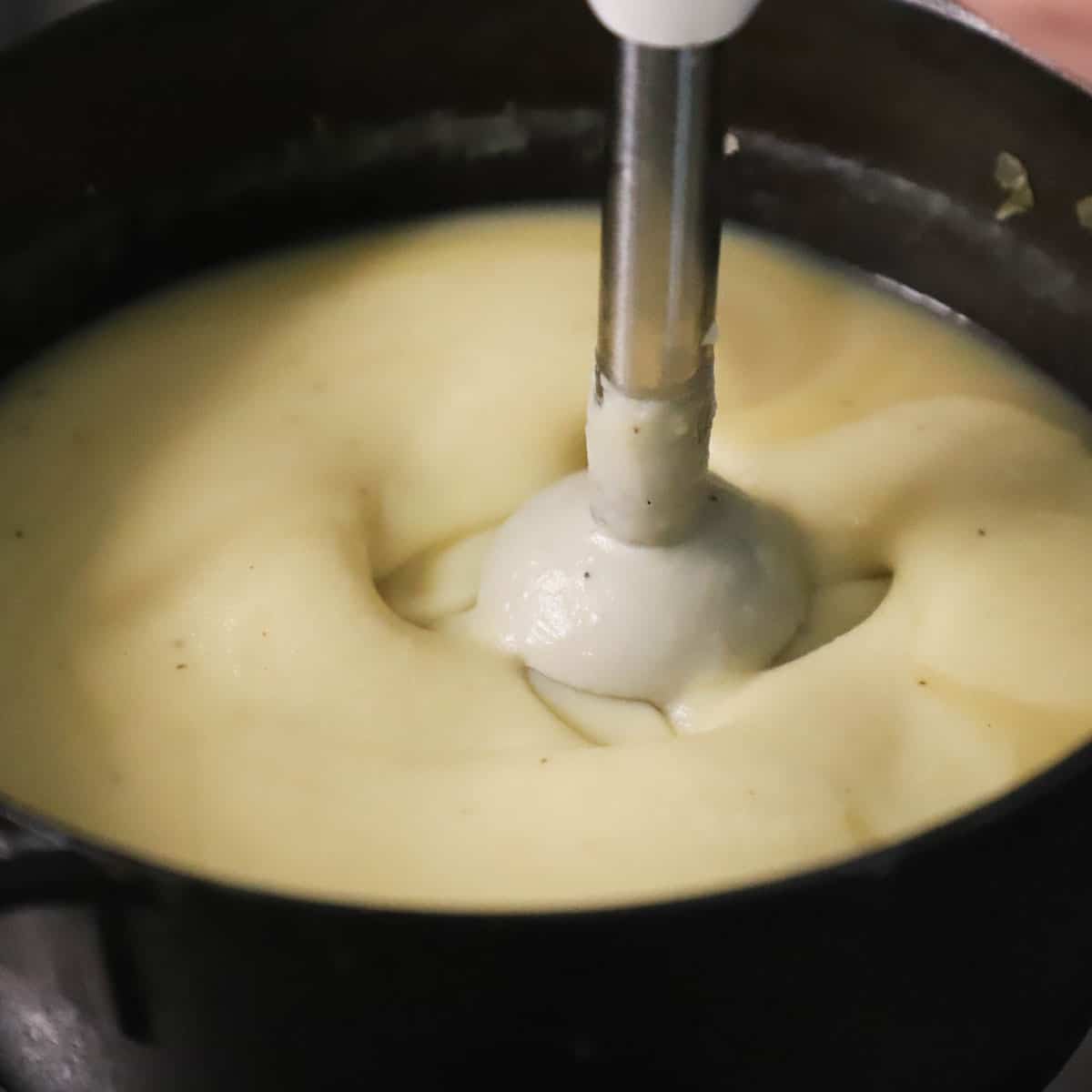 An immersion blender being used to purée potatoes for creamy Irish potato soup