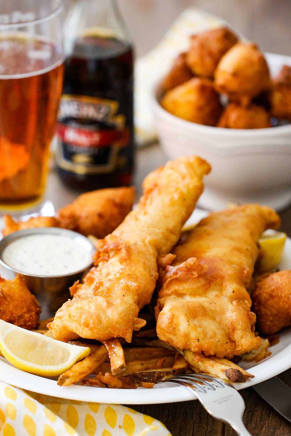 A close-up view of a plate of classic fish and chips with a small vessel of tartar sauce nearby.