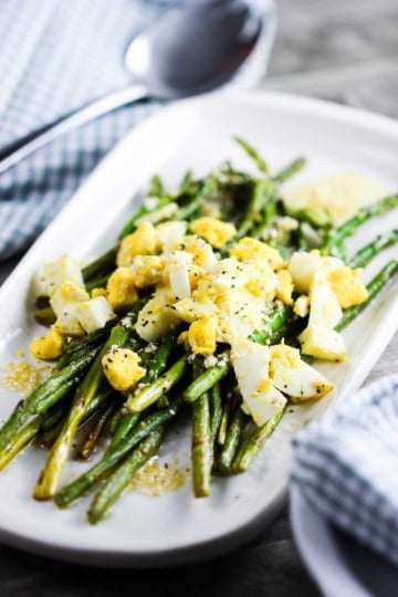 A white platter filled with roasted asparagus with chopped egg on top.